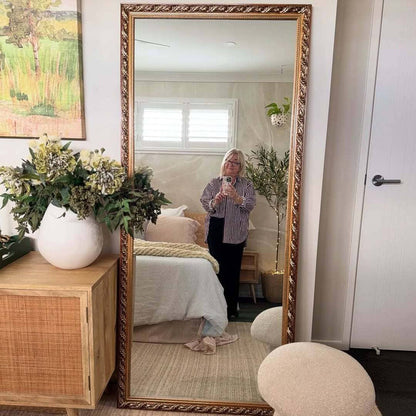 Person taking a photo of themselves in a large decorative mirror in a bedroom.