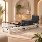 Foldable aluminium Pilates reformer with black PU leather cushions, sitting box and jump board in a warm living room