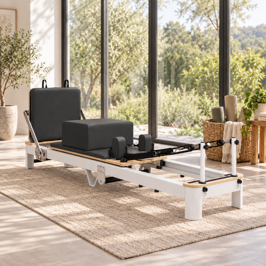 Black and white Pilates reformer with sitting box, shoulder rests and jump board beside large garden windows